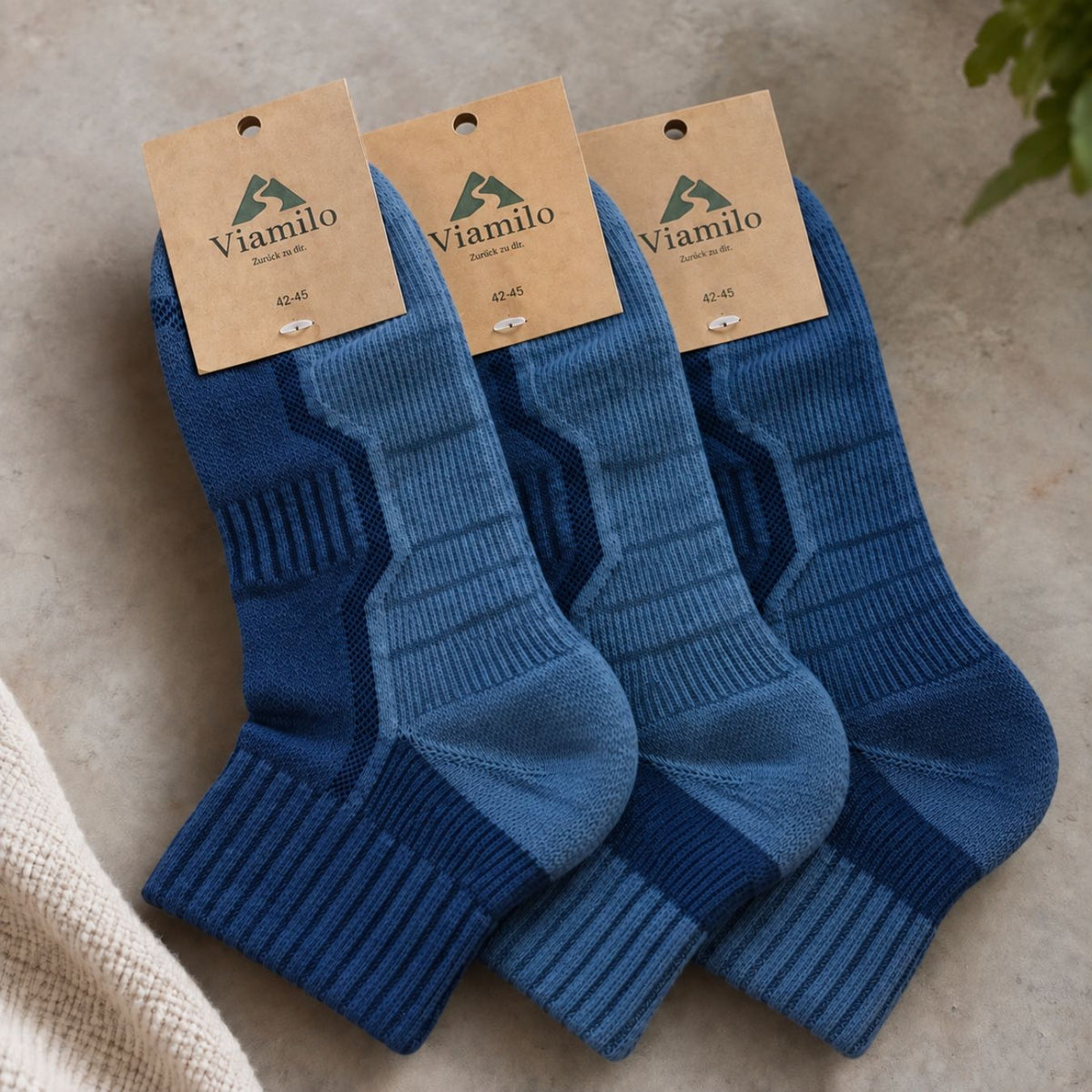 Drei Paar blaue Merino-Wandersocken von Viamilo mit Produktetiketten auf hellem Hintergrund