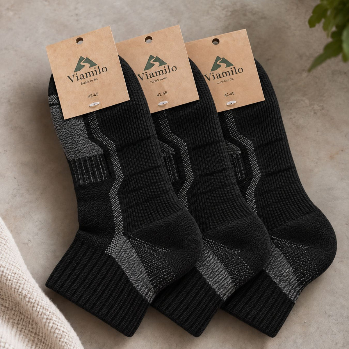 Drei Paar schwarze Viamilo Merino-Wandersocken mit Produktetiketten auf hellem Hintergrund