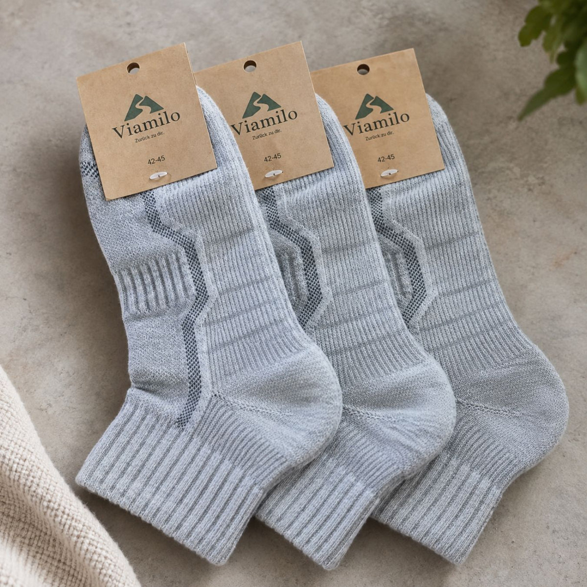 Drei Paar hellgraue Viamilo Merino-Wandersocken mit Produktetiketten auf hellem Hintergrund